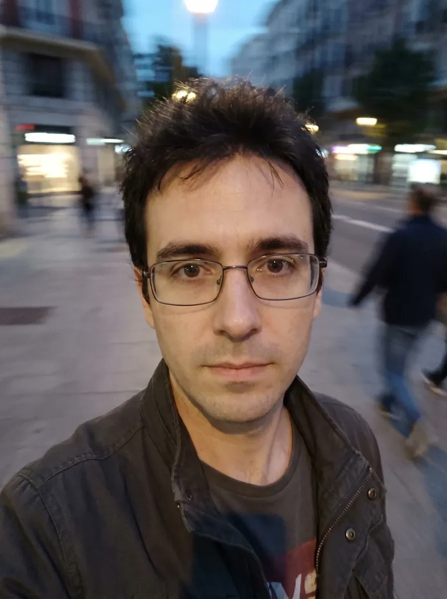 Original selfie input — man in glasses and a dark jacket outdoors in the evening